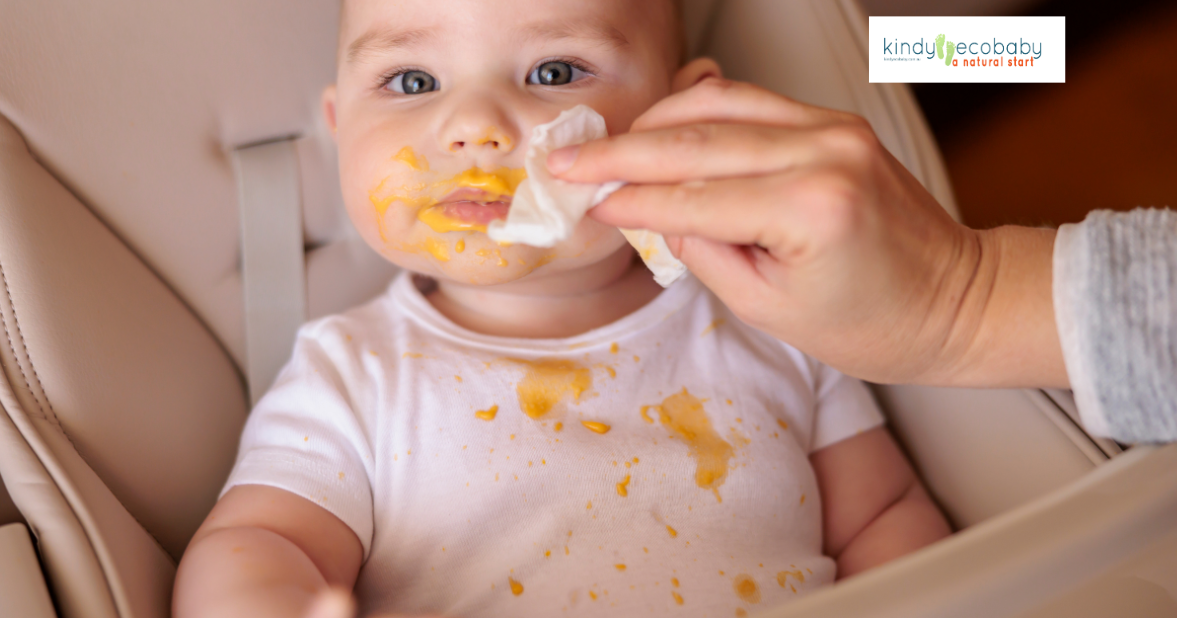 Baby with face covered in yellow food having its face wiped clean with a wet wipe