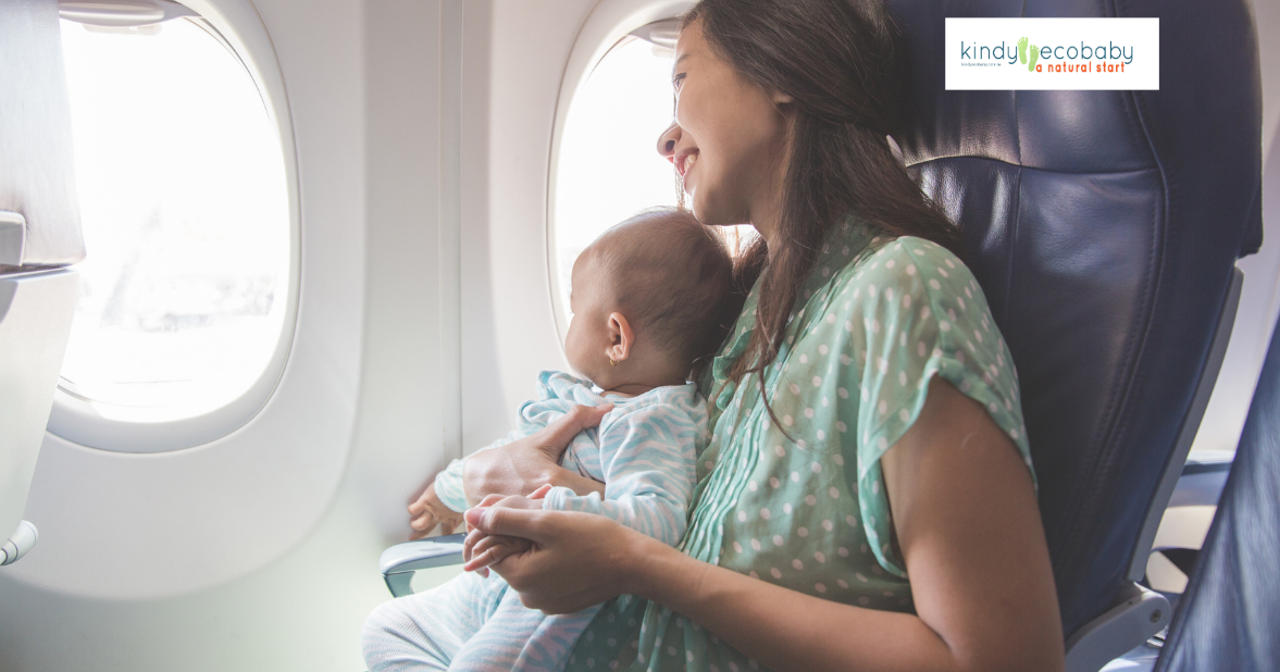Woman on a plane with a baby and smiling and looking out the window of the plane. The baby is sitting on her lap